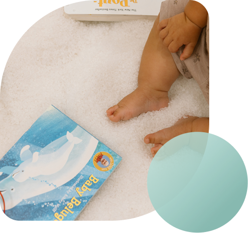 A baby sitting in a salt-covered room beside a Baby Beluga picture book.