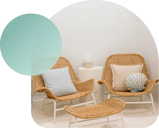 Wicker lounge chairs with ocean-themed seashell pillows in a salt therapy room.