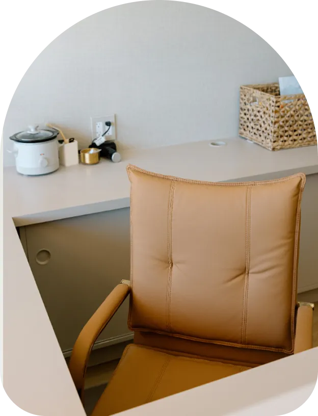 A tan leather desk chair positioned in front of a white counter with various wellness supplies and a wicker basket.