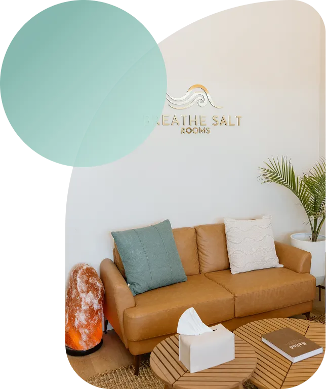 The reception area of Breathe Salt Rooms featuring a tan leather sofa, a large Himalayan salt lamp, and the company logo on the wall.
