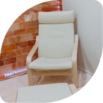 Wicker lounge chairs with ocean-themed seashell pillows in a salt therapy room.
